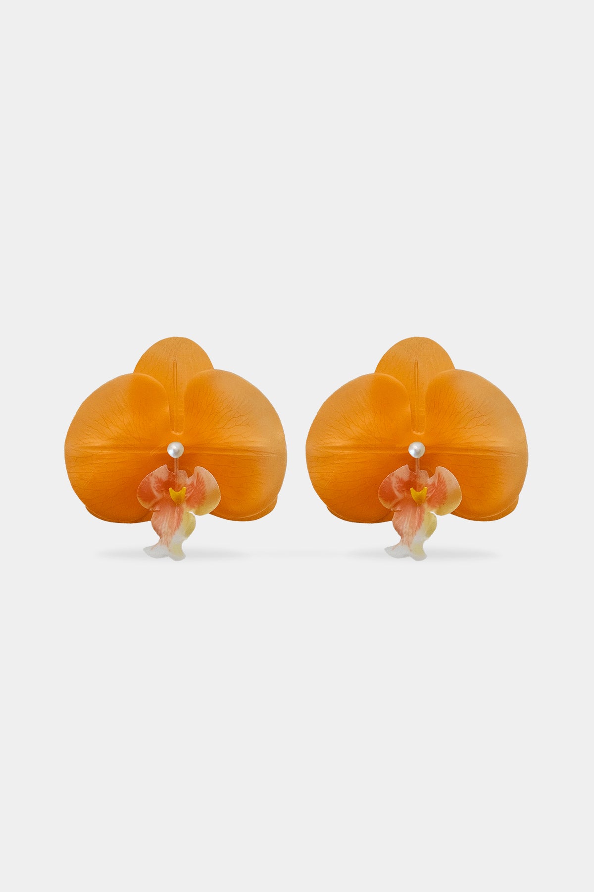 A pair of orange orchid-shaped earrings with small white pearl-like centers and delicate pink and yellow accents, displayed on a clean light gray background.